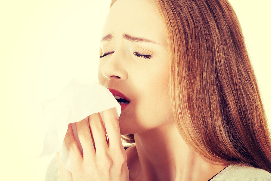 Beautiful caucasian woman sneezing, holding a tissue.